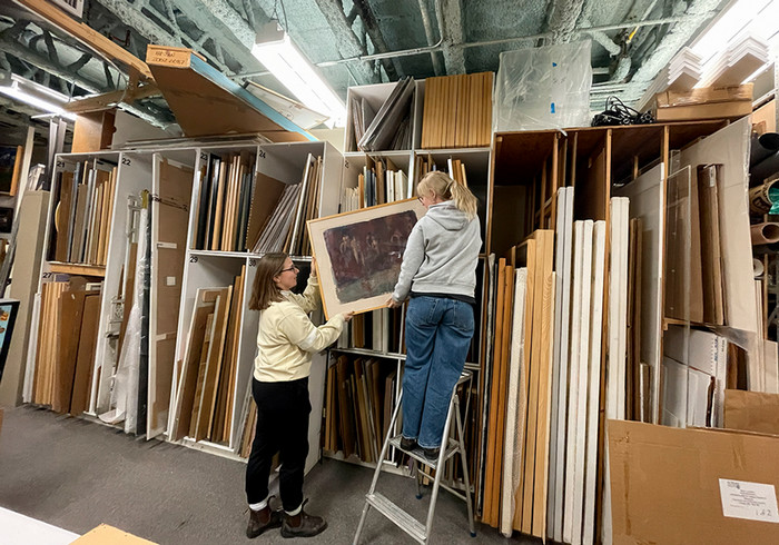 collections assistant emily henry and collections volunteer kath goodhue lift an artwork from the shelves in the vault